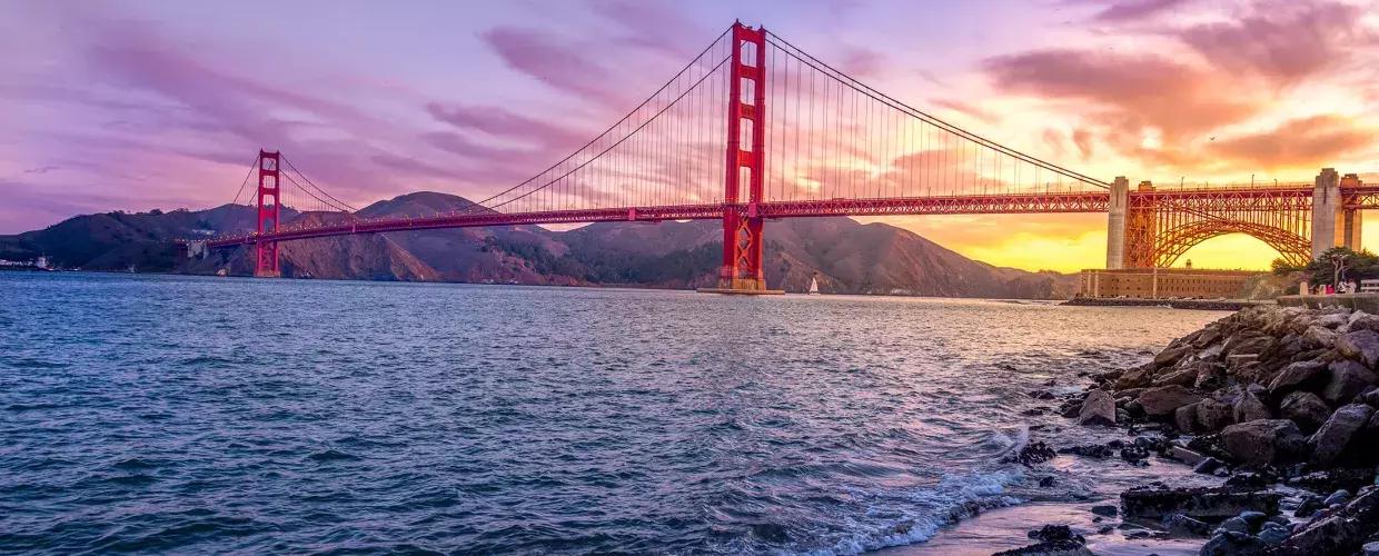 The Golden Gate Bridge at sunset with a multicolored sky 和 the San Francisco Bay in the foreground.